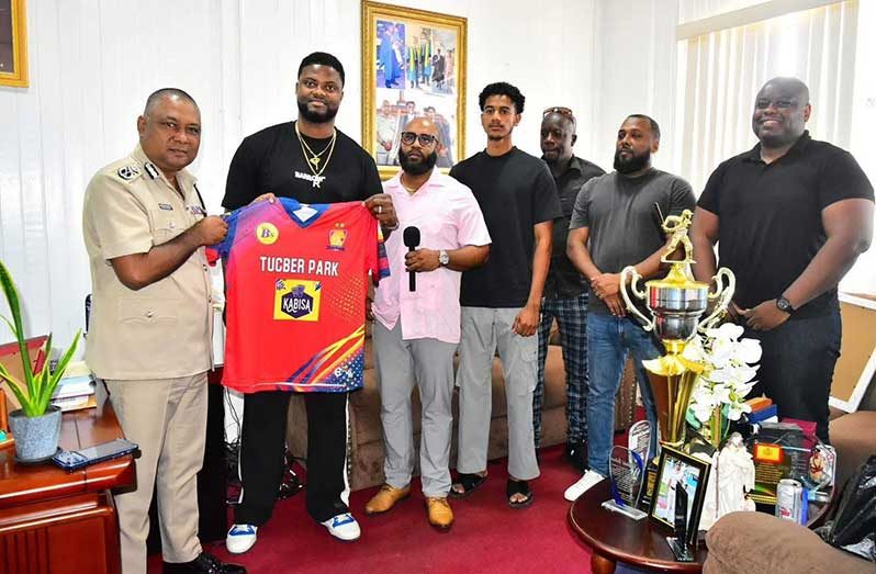 Romario Shepherd hands over club jersey to Deputy Commissioner Budhram in the presence of other club officials