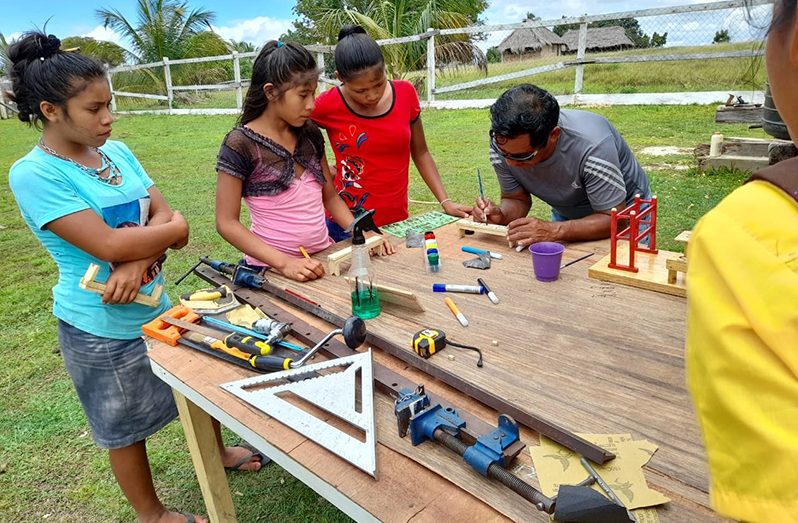 Uncle Theodore Edwards teaches young girls how to craft wood in Maruranau Village