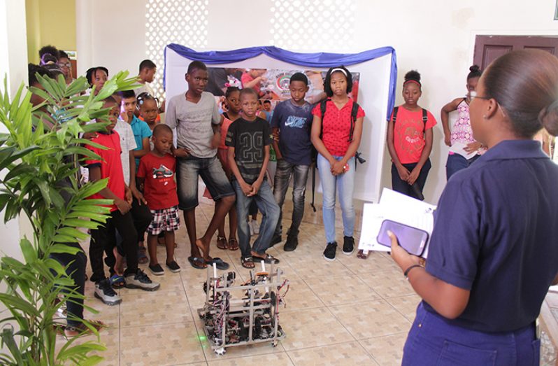 Children at the ‘Reading and Robotics’ programme at the National Library, looking on at a demonstration of the STEM Guyana robot that participated in the First Global Robotics championships this year (Vishani Ragobeer photo)