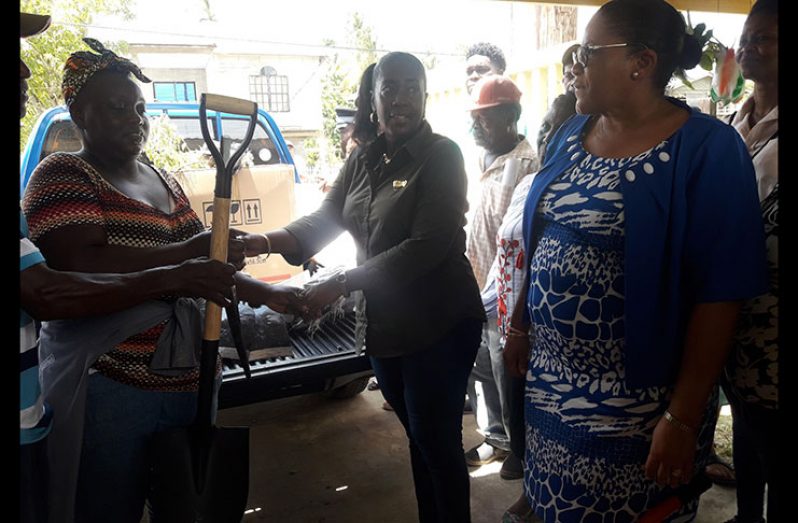 A member of the Sandvoort Farmers Society receives agricultural tools from Junior Minister Of Agriculture, Valarie Yearwood-Patterson, as Regional Executive Officer, Kim Williams-Stephen looks on