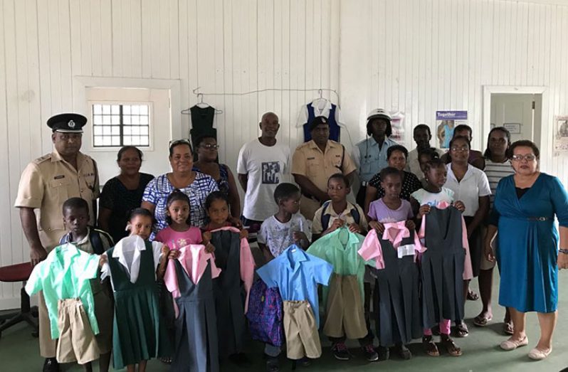 (From Left rear) Commander Budhram, parents, teachers police ranks and students from various schools hold up their new school uniforms that were handed over at the Byderabo Multipurpose Complex, Bartica