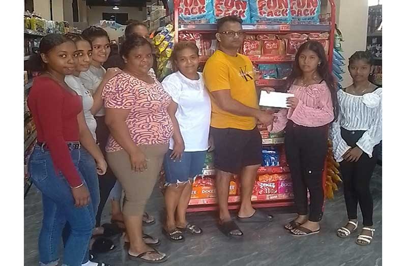 Representative of R.S. Sports, Ms. Assriya Seetaram (right), receives sponsorship cheque from Deonarain of J&G Supermarket while other staff members look on