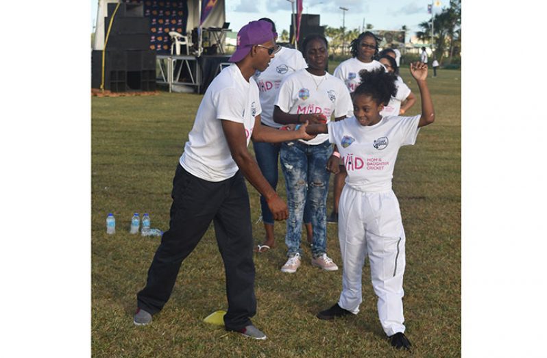 Shivnarine Chanderpaul assists a young participant with the art of bowling on Saturday at the St Stanislaus College ground. (John Ramsingh photo)