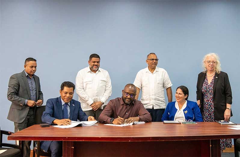 Permanent Secretary at the Ministry of Health, Malcolm Watkins (seated at centre) and Managing Director of RioMed Limited (seated first from left) sign the contract in the presence of IDB’s Country Representative, Lorena Solorzano Salazar (Seated first from right), Minister of Health, Dr Frank Anthony (standing second from right) and British High Commissioner (first from right) (Delano Williams photo)