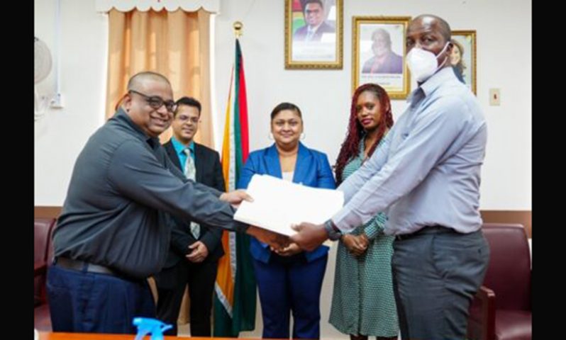 Permanent Secretary, Alfred King and Adrian Singh of Gafsons Industries Limited shake hands after signing contract documents and Education Minister, Priya Manickchand (centre), Director of NCERD, Quenita Walrond-Lewis (back right) and CEO of GEA, Dr. Mahender Sharma (back left) look on