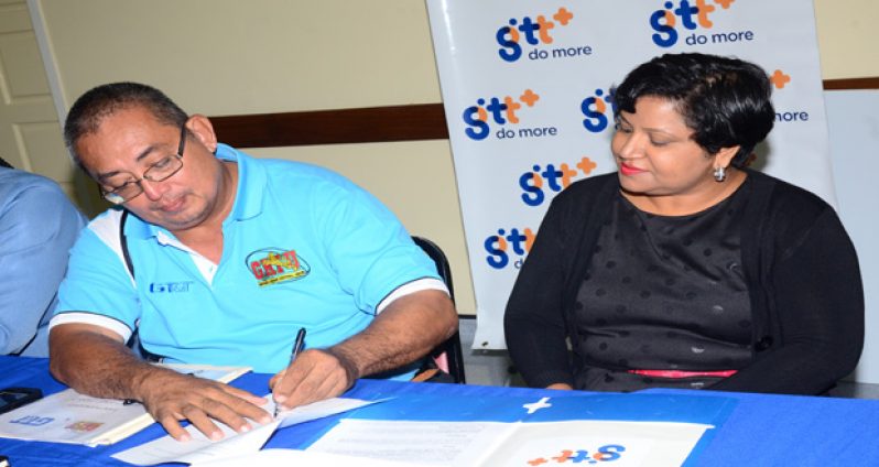 GRFU president Peter Green signs the MOU while GT&T's Senior Marketing Executive Anjanie Hackett looks on. (Adrian Narine photo)