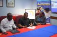 Petra Co- Director, Troy Mendonca (centre), signs the document in the presence of Petra Representative, Troy Peters (left) and Sales and Marketing coordinator at The Demerara Mutual Group, Oceola Van Doimen (right)