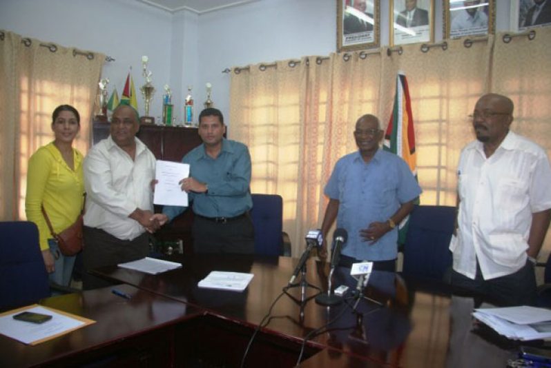 Permanent Secretary, Ministry of Local Government Mr Collin Croal hands over the Memorandum of Understanding (MOU) to Natural Globe Incorporated’s Chief Executive Officer, Mohamed Osman, in the presence of Minister Ganga Persaud and Minister  Norman Whittaker