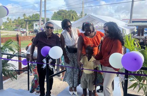 Minister of Local Government and Regional Development, Sonia Parag, assists a young resident in cutting the ceremonial ribbon to officially open the new Hogstye/Lancaster NDC administration building on Sunday.