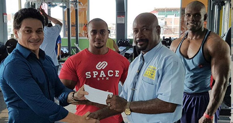 Manager of Space Gym, Mr Sergio Matos, hands over the one-year sponsorship contract to Producer of Maximum Sports Combat and Strength, Mr Max Massiah, while Roger Callender, Powerlifting champion & coach, and a gym member look on.