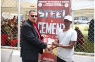 Minister of Housing and Water, Collin Croal, hands over a voucher to a beneficiary