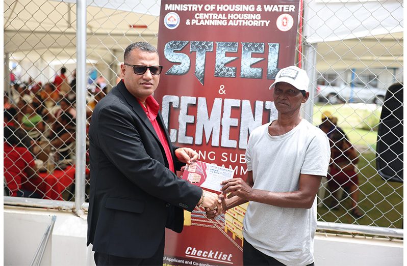 Minister of Housing and Water, Collin Croal, hands over a voucher to a beneficiary