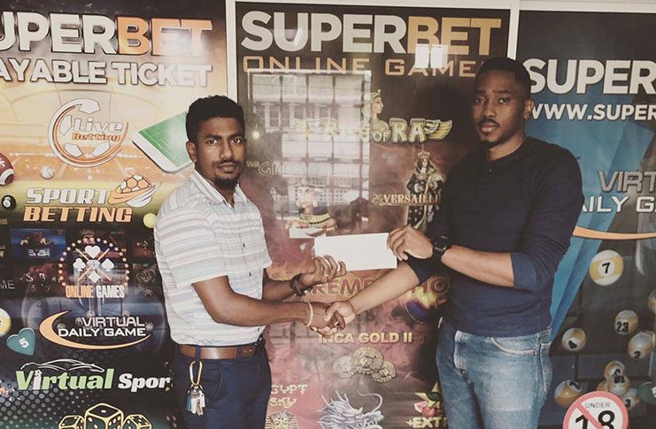 Dwight Dodson (left) collects a cheque from a Superbet Guyana representative.