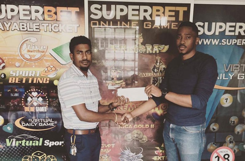 Dwight Dodson (left) collects a cheque from a Superbet Guyana representative.