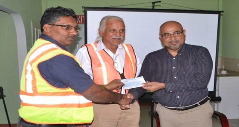 Co-Chairman of CGX Energy Inc., Professor Suresh Narine handing over the cheque to Gaico Construction Inc., Managing Director, Komal Singh in the presence of the Ministry of Public Infrastructure’s Technical Advisor, Walter Willis at the CGX New Market Street Office yesterday