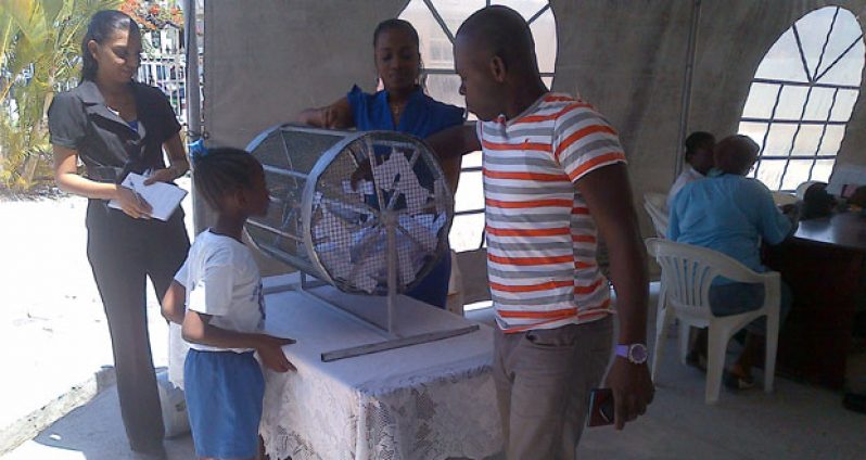 A member of the Public puts his hands into the cage with the names of persons who would have submitted declarations to the GRA