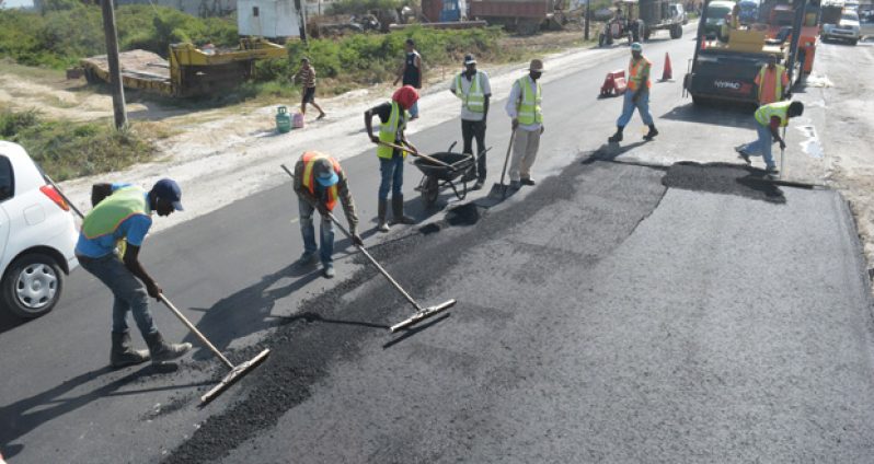 Workmen level asphalt placed on the road as part of the quality testing process