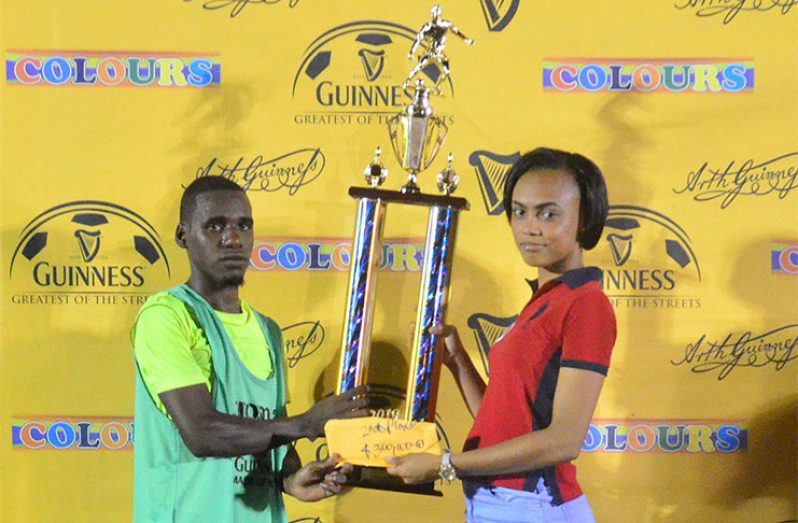 Albouystown-B’s Lennox Cort receives the second placed trophy and prize from a Colours Boutique representative.