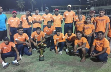 We are still the champions! The victorious orange clad Universal DVD Berbice Titans strikes a pose with their spoils and Chief Executive Officer of Universal Solutions and Universal DVD Store Vicram Seubarran (stooping at right). Coach Julian Moore is at left (blue jersey).