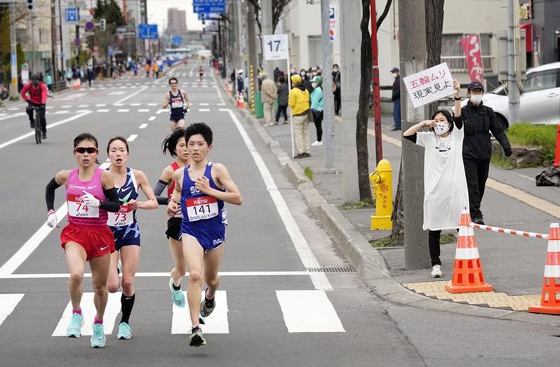 A spectator raises a paper sign reading: 'It is impossible to hold the Olympics, face up to reality' along the race route during the half-marathon as part of Hokkaido-Sapporo Marathon Festival 2021, a testing event for the Tokyo 2020 Olympics marathon race, amid the coronavirus disease (COVID-19) pandemic, in Sapporo, Hokkaido Prefecture, Japan May 5, 2021, in this photo released by Kyodo. Kyodo/via REUTERS.