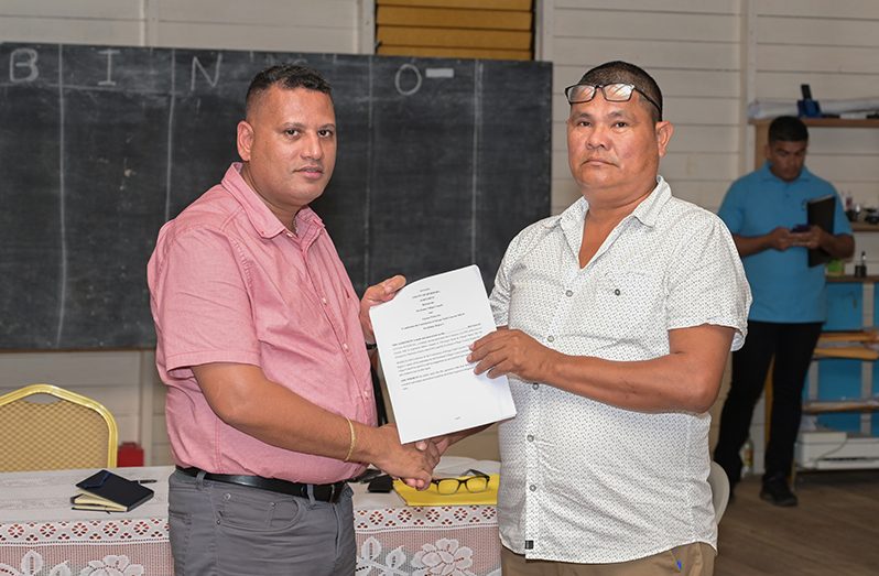 Minister of Housing and Water, Collin Croal, hands over the contract to Toshao of Kwebanna Village Council, Troy Peters