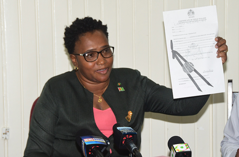 Minister of Housing, Annette Ferguson, holds a copy of the transport of the single plot of land she received after 2015 to build her property