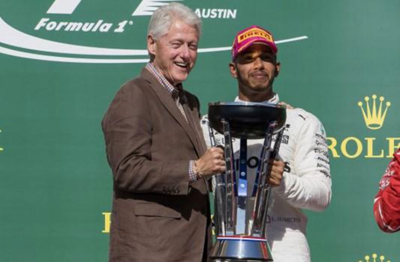 Former US President Bill Clinton hands off the trophy to Mercedes driver Lewis Hamilton (44) of Great Britain after Hamilton wins the United States Grand Prix .