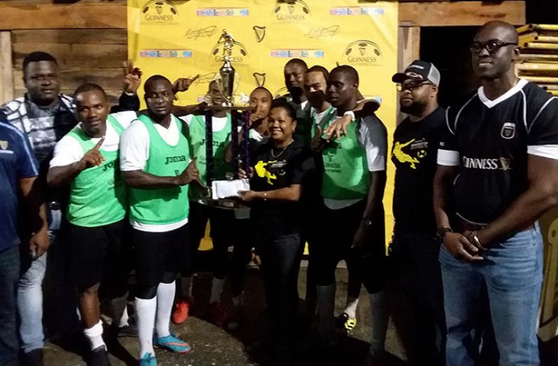 Beacons captain Whitney Welcome collecting the championship trophy from Banks DIH Bartica Branch Manager, Amanda Murray, in the presence of his team-mates. Also in photo is Lee Baptiste (extreme right), Guinness Brand Executive, and Bartica District Sales Supervisor, Keron Savory.