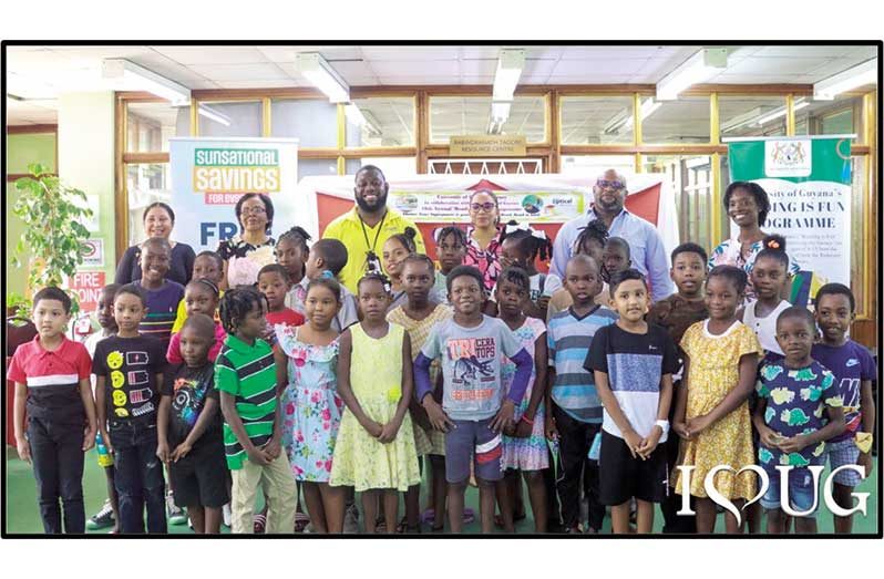 Last row from left: Vice-Chancellor, Professor Paloma Mohamed Martin and UG's Chief Librarian, Mrs Gwyneth George; second from right, Courts Optical Chain Manager, Mr Richard Simpson, along with other UG and Unicomer staff and some of the children who will be participating in this year’s "Reading is Fun" Programme (UG photo)