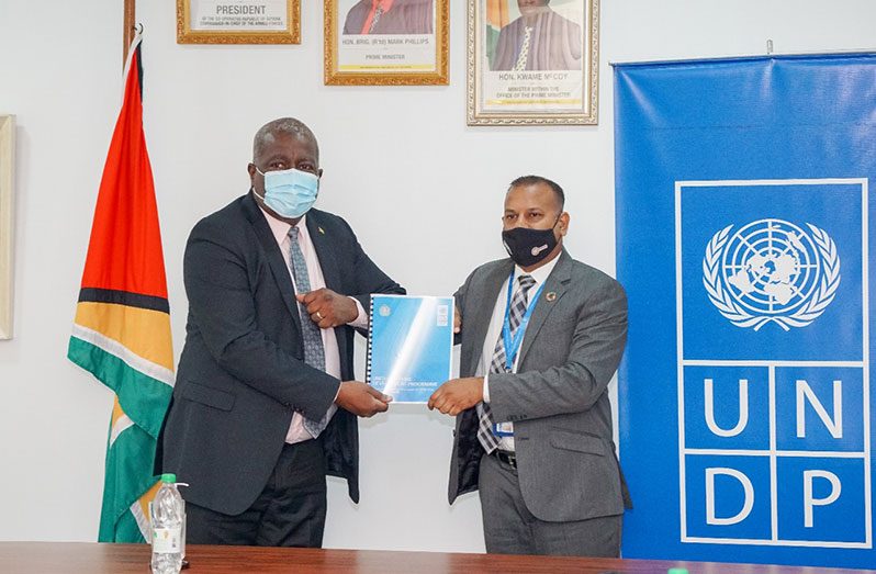 Prime Minister, Brigadier (ret’d) Mark Phillips receives a copy of the socio-economic impact assessment report from Operations Coordinator UNDP Guyana, Navindra Persaud