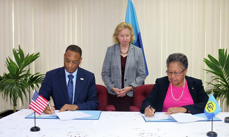 CARICOM Secretary-General, Dr Carla Barnett (right) and USAID’s Regional Representative for the Eastern and Southern Caribbean, Clinton D. White (left) sign the agreement as Ambassador Sarah-Ann Lynch looks on (US Embassy photo)