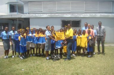 St Stanislaus College’s Sixth Form student Kendra Warner hands over the uniforms and boots to West Ruimveldt Primary School teacher Petal Lashley in the presence of students from both schools.