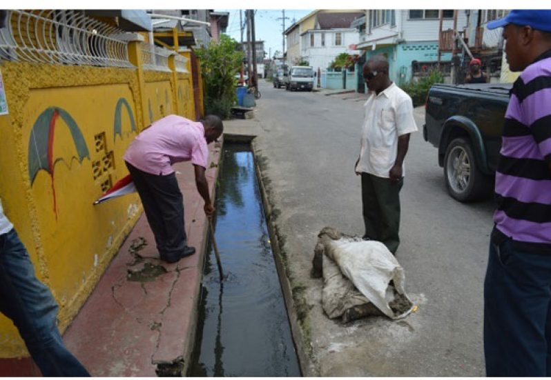 Engineer inspects a cleaned drain in Albouystown