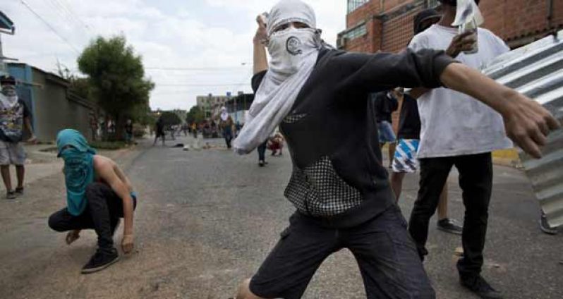 Masked demonstrators engaging riot police Wednesday in Valencia, some 105 miles west of the capital, Caracas (Photo courtesy of AP)