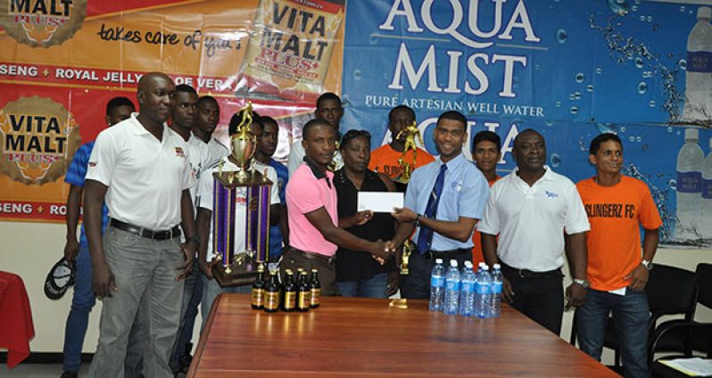 Aqua Mist Brand Manager Errol Nelson (4th right) hands over the sponsorship cheque to WDFA President Nigel Garraway. Also present of Vita Malt Brand Manager Clayton McKenzie, Communications Manager Troy Peters, players and other officials.