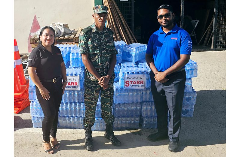 Marketing Manager Penny Francis (at left) and Operations Manager of Starr Computers Raydon Samaroo (at right) delivered the cases of water to Captain Drake at GDF Base Camp Ayanganna, Thomas Lands, Georgetown