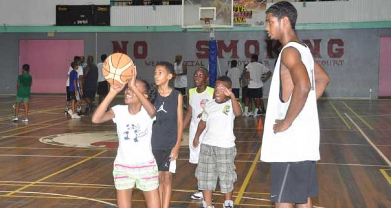 National point guard Akeem Kanhai looks on as a YBG camp participant tries to execute what she was taught (Delano Williams photo)