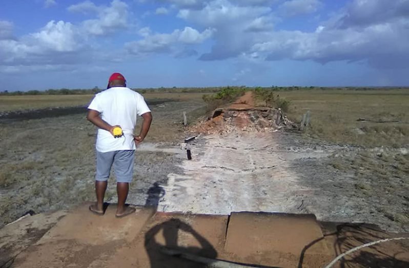 A man stands at the edge of what remains of the Yupukari Number Two bridge,  which was destroyed by fire several days ago.