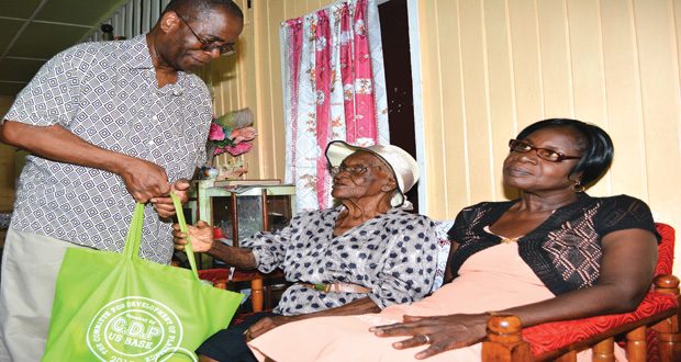 Mrs Esme Springer, now 102, receives her hampers from Mr Claude Ince of the U.S. arm of the Plaisance Community Development Group. Her devoted daughter Hazel David is seated at her left