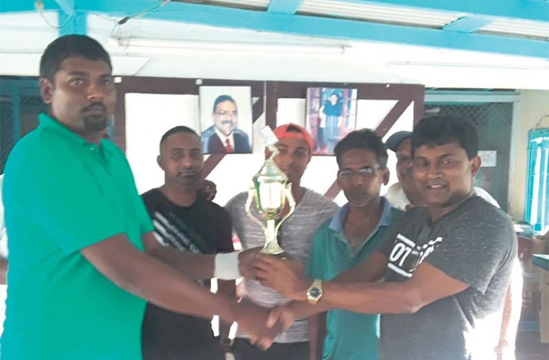 Satram Jagmohan (left) hands over the winning trophy to Basdeo Persaud in the presence of other team members.