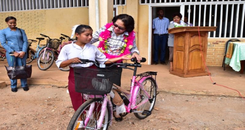 This shy First Former of the North-West Secondary School holds on to her brand new, pink bicycle as First Lady, Sandra Granger, places a comforting hand on her shoulder