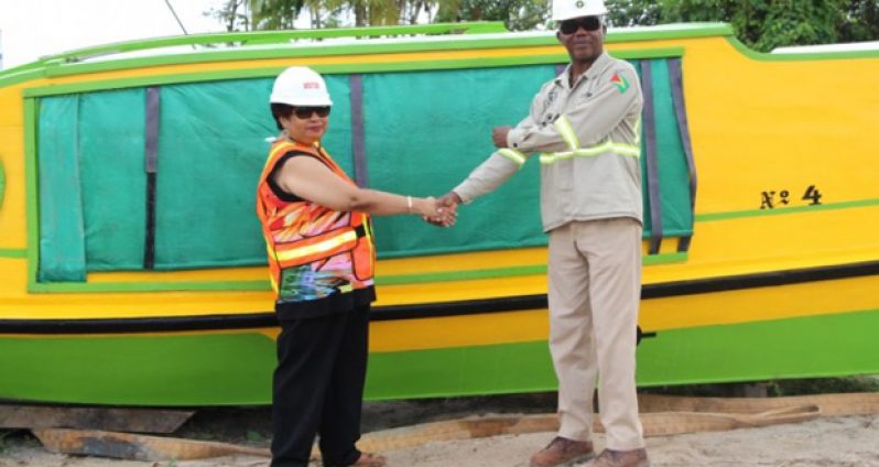 Minister of Social Cohesion Amna Ally shakes hands with Kenrick Glasgow, Logistics Manager at Guyana Goldfields Inc/Aurora Gold Project as she receives the boat the company donated to President David Granger's ''three Bs” programme to benefit school children (Ministry of the Presidency photo)