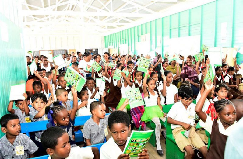 The children at Leguan excitedly hold up their books and pens, which President David Granger distributed during his visit there