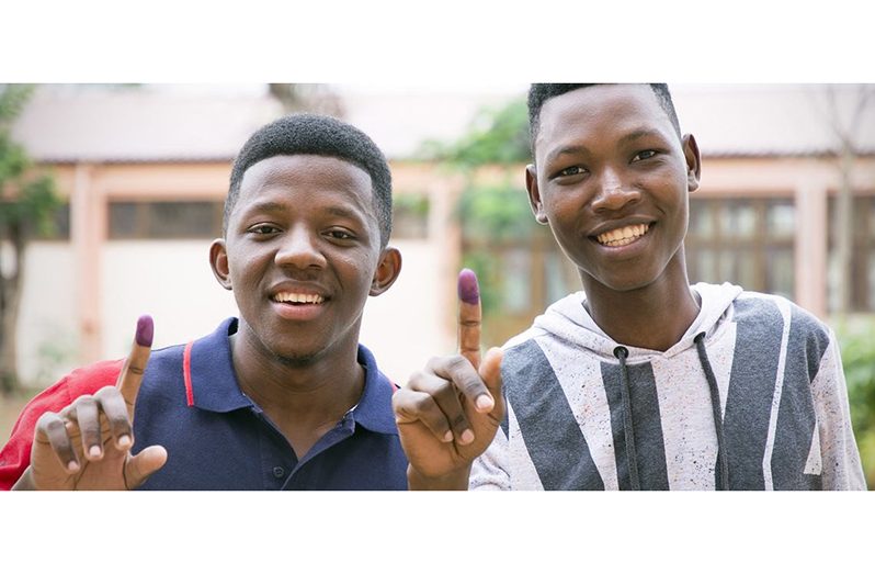 Two young men display the ink marks on their fingers, indicating  they have cast their votes in an election (UNDP/Rochan Kadariya photo)