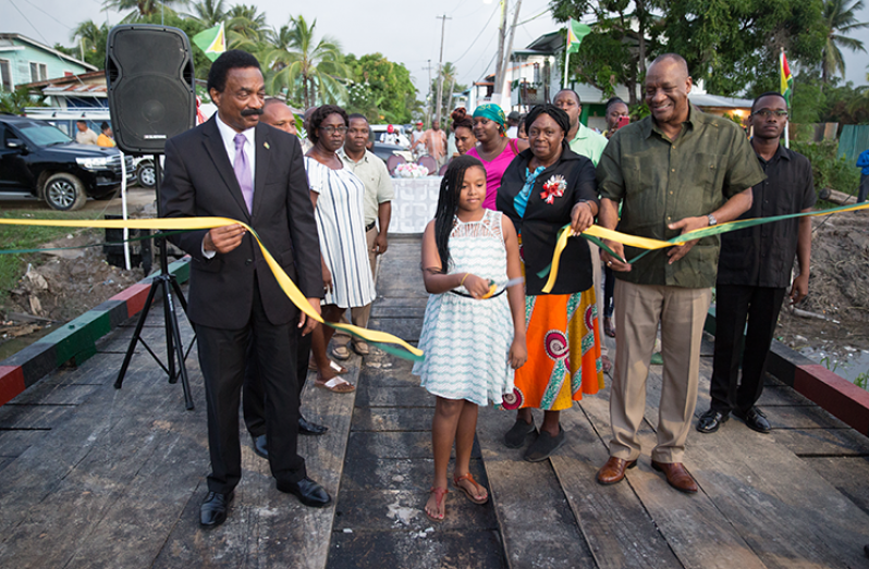Attorney General and Minister of Legal Affairs Basil Williams and Director General of the Ministry of the Presidency Joseph Harmon assist a young resident with the cutting of the ribbon