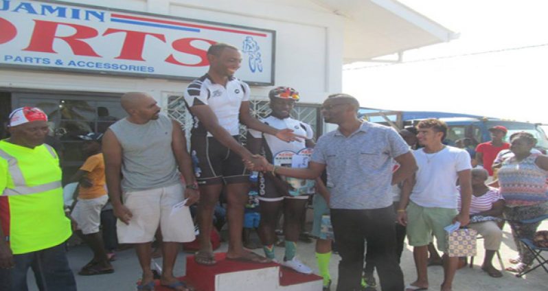 Marlon `Fishy’ Williams (at top of podium) accepts his first prize monetary award from Director of Sport Chr4istopher Jones. At Williams’ left is veteran rider and second-place finisher Robin Persaud, while at his (Williams) right is third-place finisher and team mate Orville Hinds.