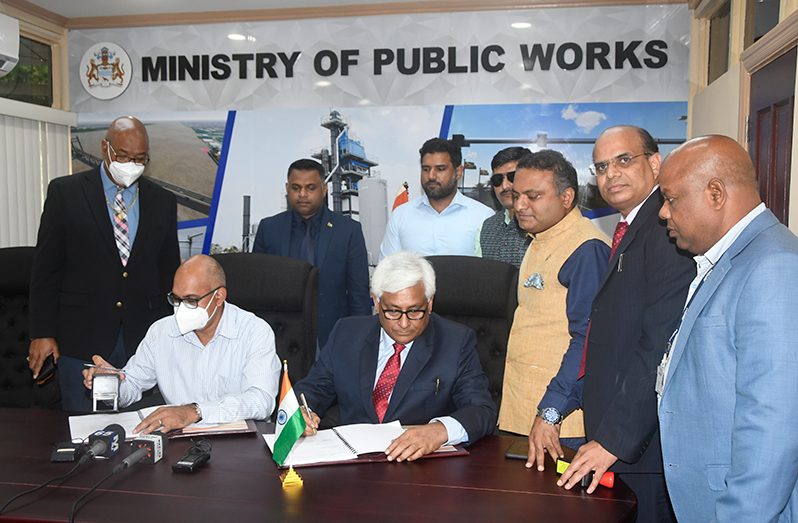 Representative of RITES Limited (seated at right) and Permanent Secretary (ag) at the Ministry of Public Works, Ron Rahaman (seated at left) sign the contract as other officials watch on (Adrian Narine photo)