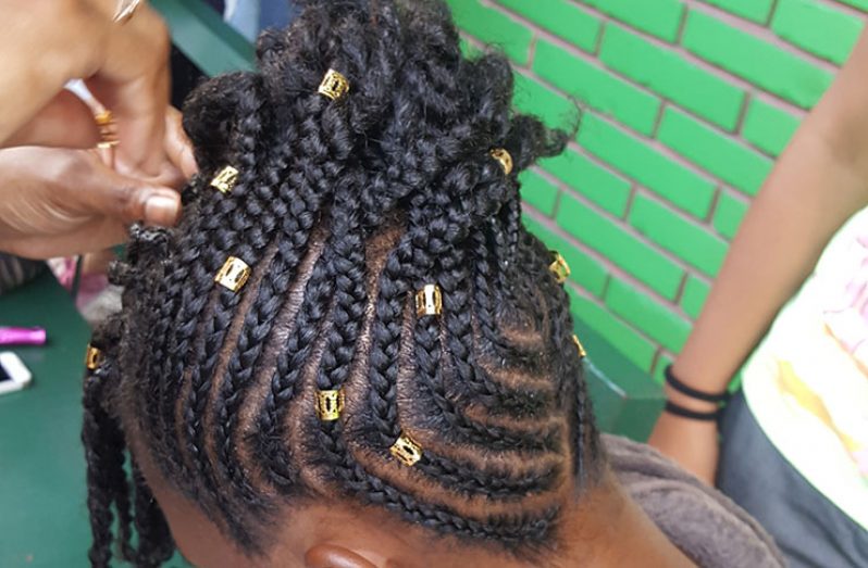 A girl receiving cornrow and braiding styles for back-to-school
