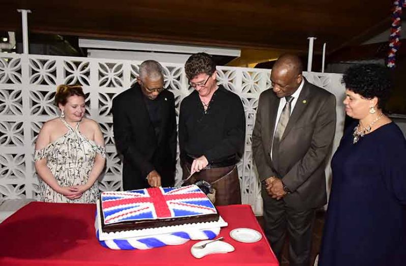 President David Granger helps British High Commissioner to Guyana, Greg Quinn cut the traditional cake in celebration of Queen Elizabeth II’s 92nd Birthday as Minister of State Joseph Harmon and other dignitaries look on Thursday (Ministry of the Presidency photo)
