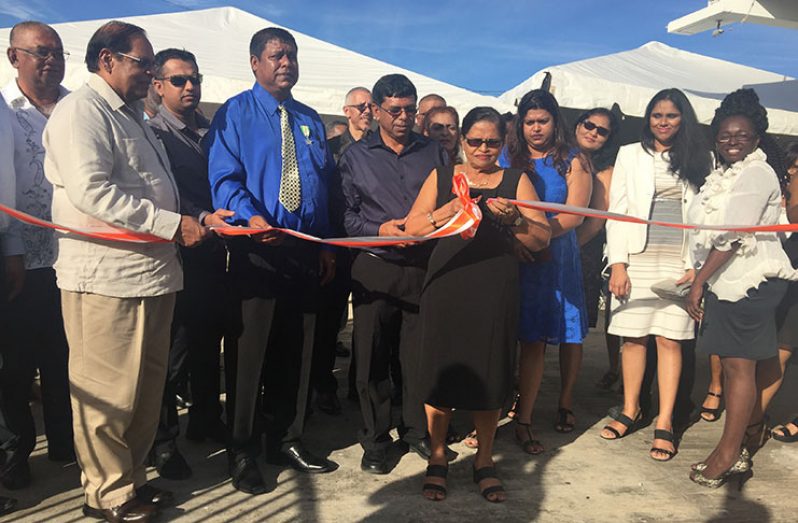 Sakuntie Persaud, wife of the late Nand Persaud with assistance from Prime Minister Moses Nagamootoo cuts the ceremonial ribbon to officially commission the $110M solar facility as family and staff look on